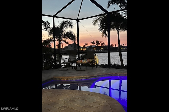 pool at dusk featuring a lanai, a water view, and a patio