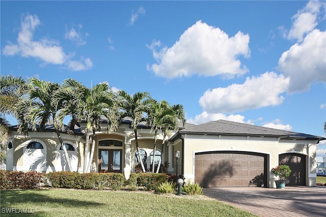 view of front of home featuring french doors, a garage, a front yard, stucco siding, and decorative driveway