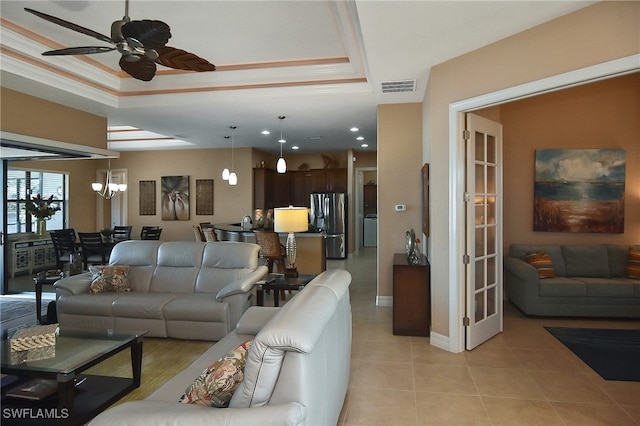 tiled living room with crown molding, ceiling fan with notable chandelier, and a raised ceiling