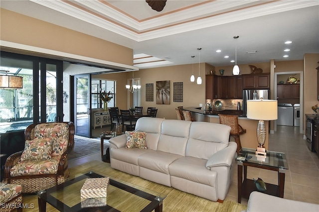 living room featuring a notable chandelier, washing machine and clothes dryer, ornamental molding, and light tile patterned floors