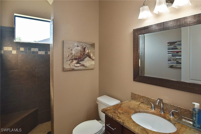 bathroom featuring toilet, vanity, and a tile shower