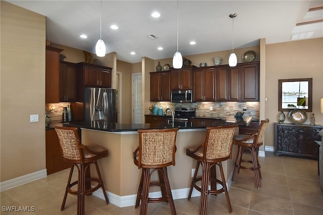 kitchen with a breakfast bar area, hanging light fixtures, appliances with stainless steel finishes, and decorative backsplash