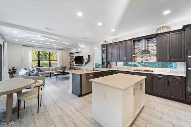 kitchen featuring a center island, wall chimney range hood, appliances with stainless steel finishes, decorative light fixtures, and kitchen peninsula