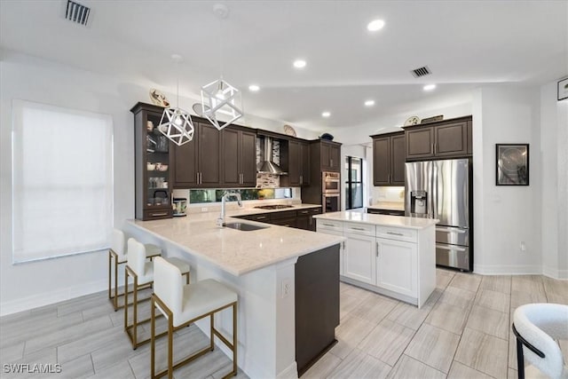 kitchen featuring appliances with stainless steel finishes, sink, wall chimney range hood, hanging light fixtures, and a breakfast bar area