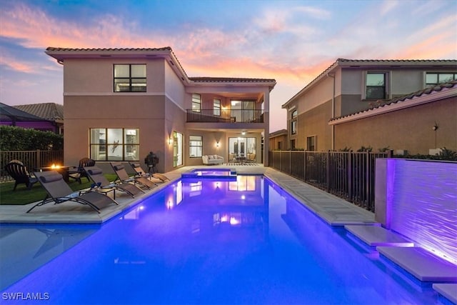 pool at dusk featuring an in ground hot tub and a patio