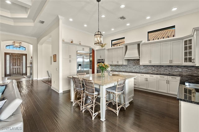 kitchen featuring premium range hood, stainless steel appliances, sink, decorative light fixtures, and dark stone countertops