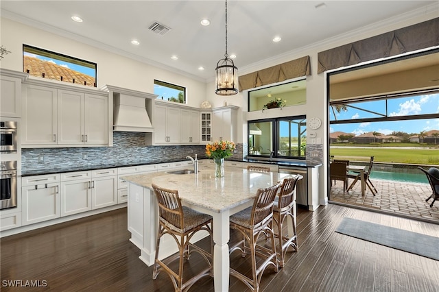 kitchen with crown molding, hanging light fixtures, light stone countertops, custom range hood, and a breakfast bar area