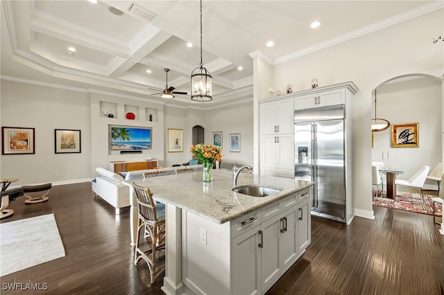 kitchen with a kitchen island with sink, coffered ceiling, built in fridge, sink, and light stone countertops