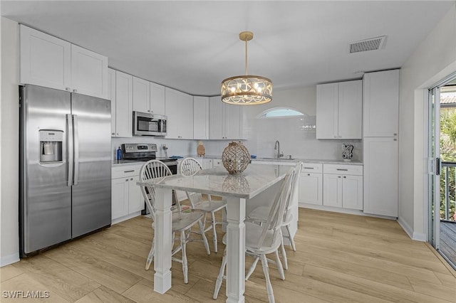 kitchen with white cabinets, sink, hanging light fixtures, light wood-type flooring, and stainless steel appliances