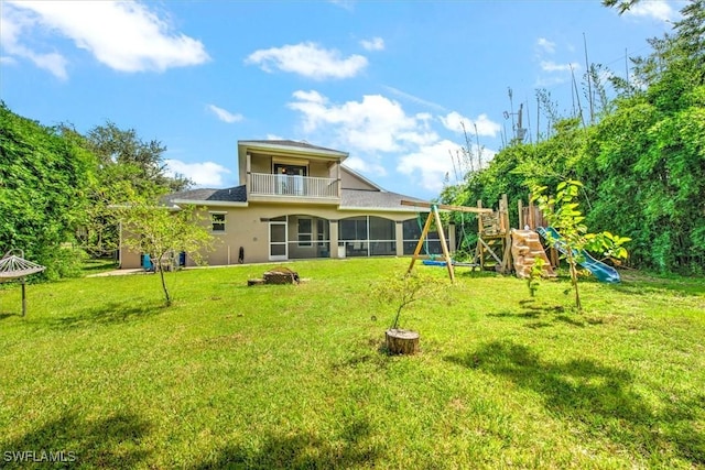 rear view of house with a balcony, a playground, and a lawn