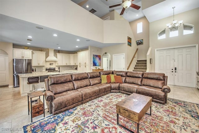 living room with ceiling fan with notable chandelier, a high ceiling, and light tile patterned floors