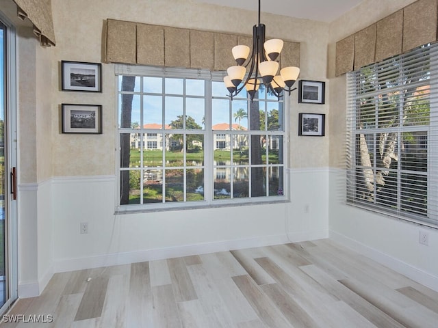 unfurnished dining area featuring a healthy amount of sunlight, light hardwood / wood-style flooring, and an inviting chandelier