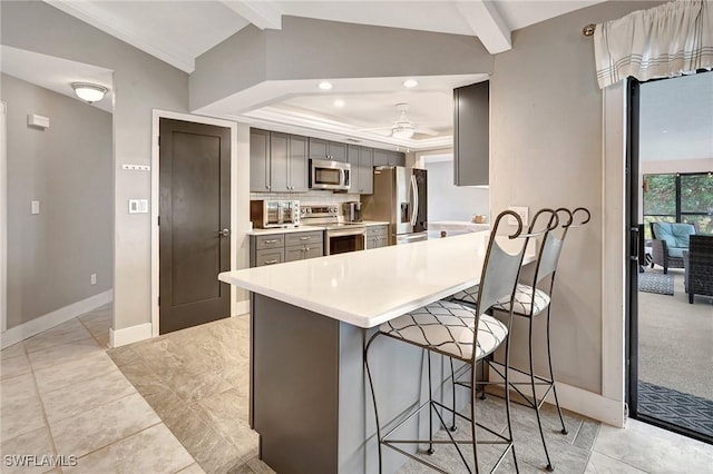 kitchen with appliances with stainless steel finishes, gray cabinetry, a kitchen breakfast bar, lofted ceiling with beams, and kitchen peninsula