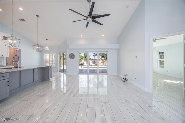 unfurnished living room featuring high vaulted ceiling, light wood-style floors, visible vents, and a sink