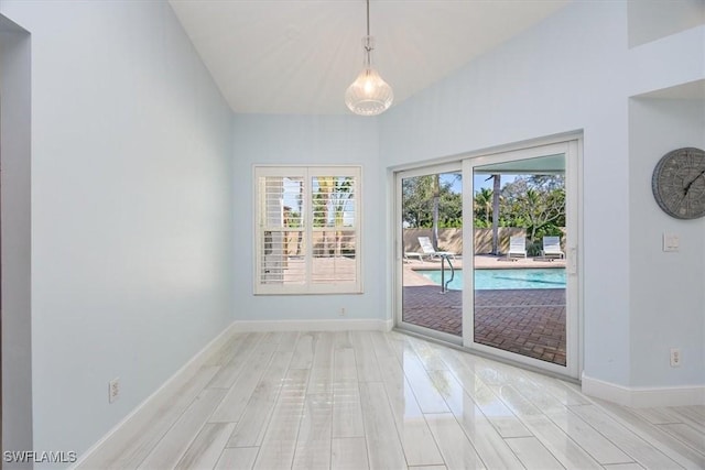 doorway with light wood-style flooring, baseboards, and lofted ceiling