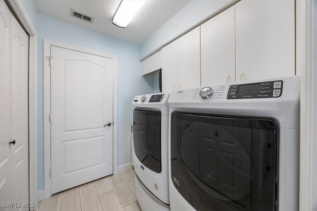 clothes washing area featuring wood tiled floor, cabinet space, visible vents, separate washer and dryer, and a textured ceiling