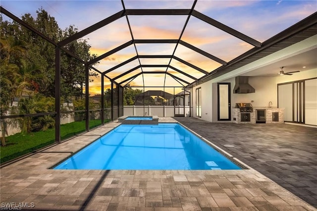 pool at dusk featuring grilling area, a lanai, an in ground hot tub, exterior kitchen, and a patio