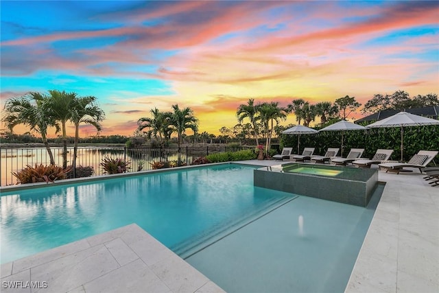 pool at dusk featuring a water view, an in ground hot tub, and a patio