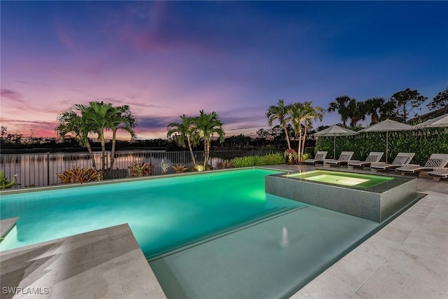 pool at dusk featuring an in ground hot tub and a patio