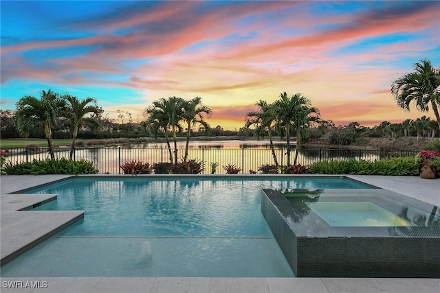 pool at dusk with an in ground hot tub and a water view