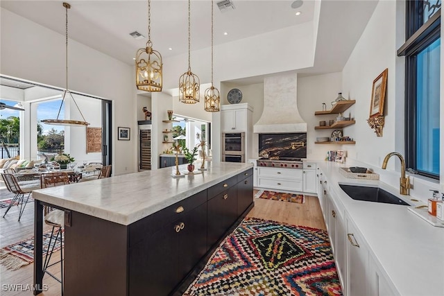 kitchen featuring a breakfast bar, white cabinets, sink, light wood-type flooring, and custom range hood