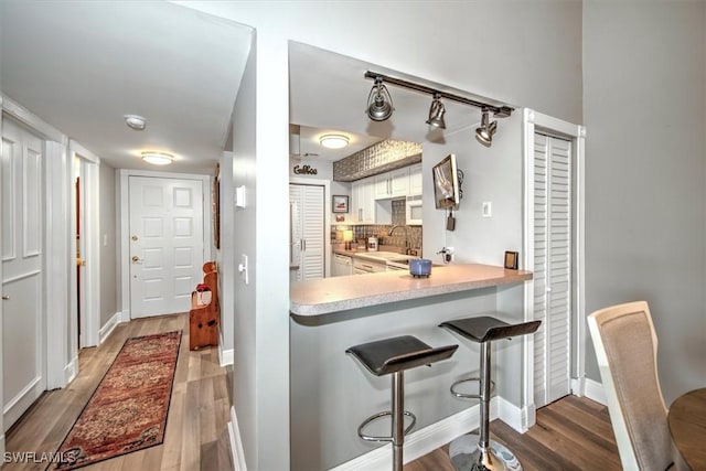 kitchen featuring white cabinetry, tasteful backsplash, kitchen peninsula, a breakfast bar, and hardwood / wood-style flooring