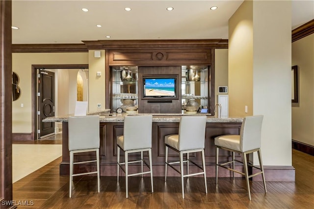 bar with light stone counters, dark wood-type flooring, and ornamental molding