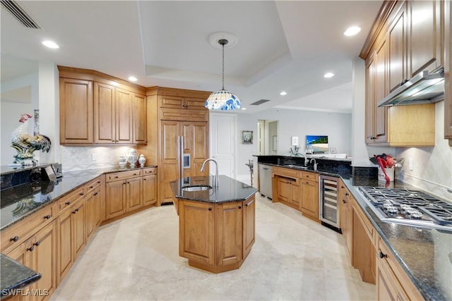 kitchen with decorative light fixtures, a center island with sink, a tray ceiling, stainless steel appliances, and beverage cooler