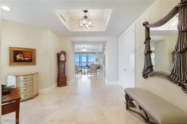 hall featuring crown molding, a tray ceiling, and an inviting chandelier