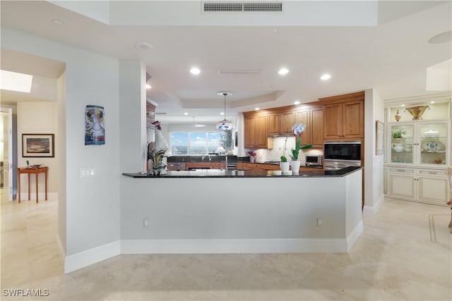 kitchen with a raised ceiling, black microwave, decorative light fixtures, and kitchen peninsula