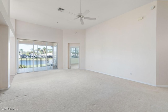 empty room featuring a water view, ceiling fan, light carpet, and a high ceiling