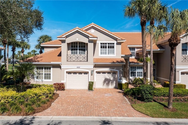 mediterranean / spanish house featuring a tiled roof, decorative driveway, an attached garage, and stucco siding