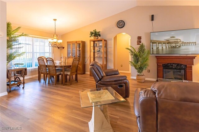 living room featuring a high end fireplace, hardwood / wood-style floors, vaulted ceiling, and a notable chandelier