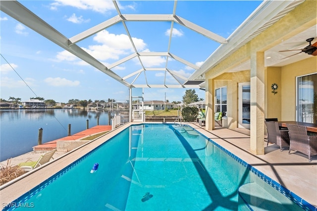 view of pool with a patio, ceiling fan, glass enclosure, a water view, and a dock