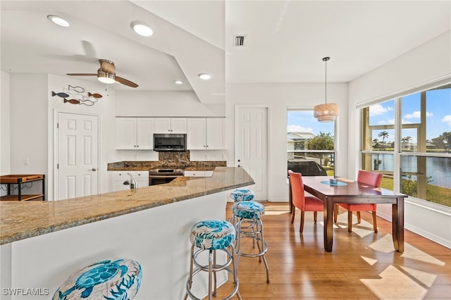 kitchen featuring white cabinetry, decorative light fixtures, appliances with stainless steel finishes, light stone countertops, and backsplash