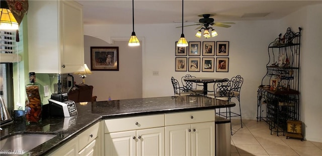 kitchen featuring white cabinetry, ceiling fan, hanging light fixtures, dark stone countertops, and light tile patterned floors