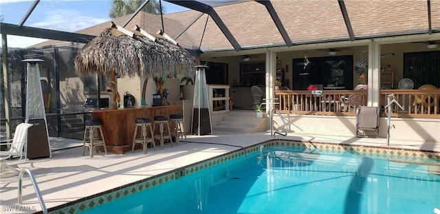 view of pool with glass enclosure, an outdoor bar, ceiling fan, and a patio area