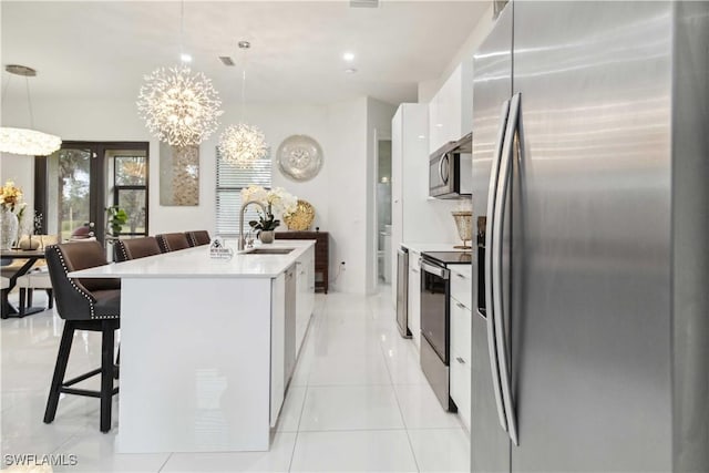 kitchen with an inviting chandelier, white cabinetry, a center island with sink, appliances with stainless steel finishes, and decorative light fixtures