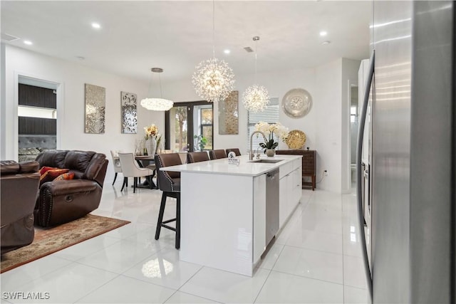 kitchen with light tile patterned floors, stainless steel appliances, a center island with sink, and hanging light fixtures