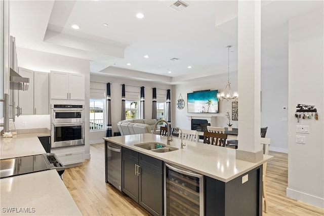 kitchen featuring pendant lighting, a center island with sink, wine cooler, a tray ceiling, and white cabinetry