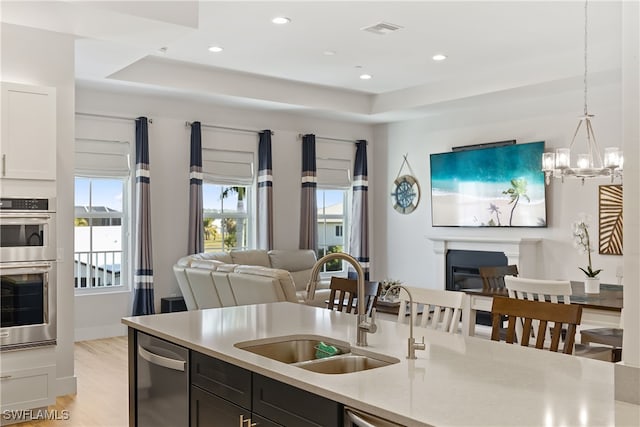 kitchen featuring light hardwood / wood-style flooring, a raised ceiling, hanging light fixtures, and sink