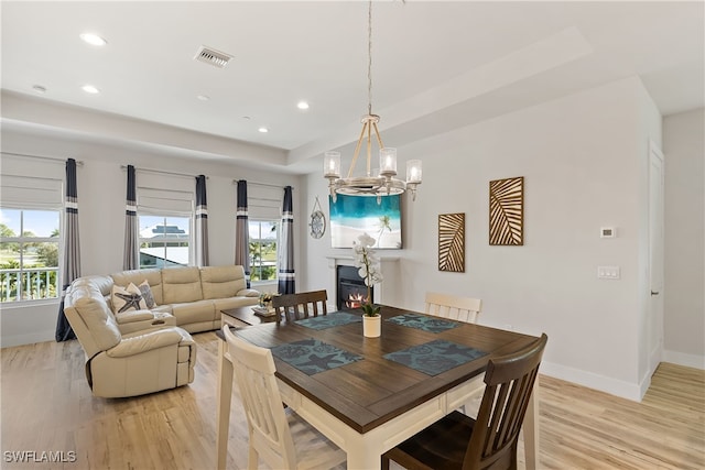 dining room with a raised ceiling, light hardwood / wood-style floors, and an inviting chandelier