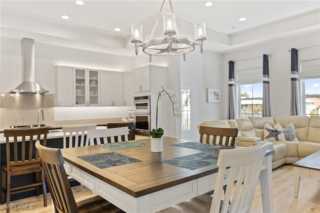 dining area featuring a tray ceiling, sink, light wood-type flooring, and an inviting chandelier