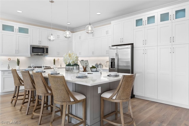 kitchen featuring appliances with stainless steel finishes, a center island with sink, white cabinets, hanging light fixtures, and a breakfast bar area