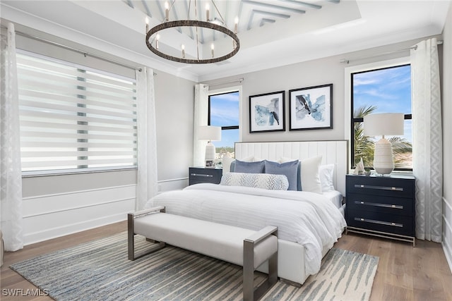 bedroom with a tray ceiling, multiple windows, hardwood / wood-style floors, and an inviting chandelier