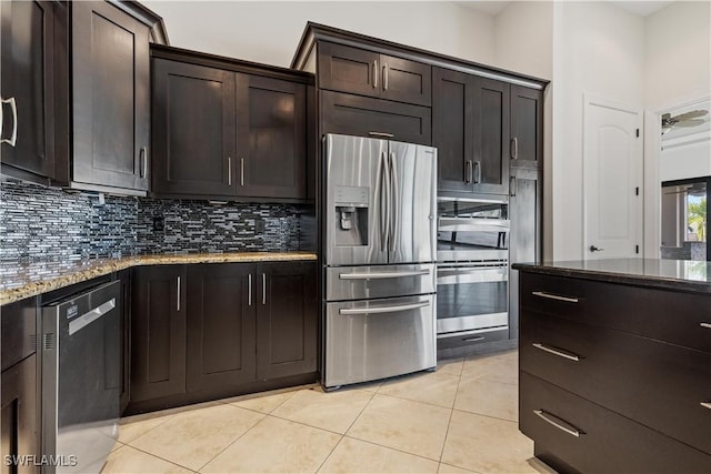 kitchen featuring decorative backsplash, appliances with stainless steel finishes, light stone countertops, dark brown cabinets, and light tile patterned floors