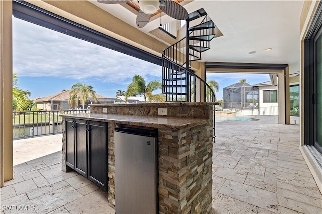 view of patio / terrace featuring a fenced in pool, a water view, ceiling fan, and a bar