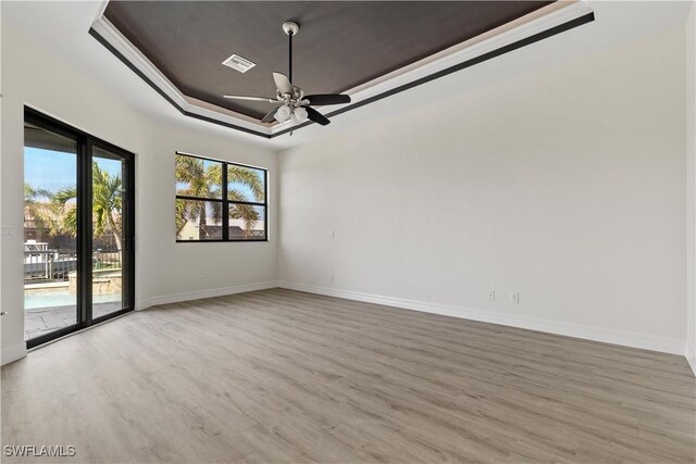 unfurnished room with a raised ceiling, ceiling fan, and light wood-type flooring