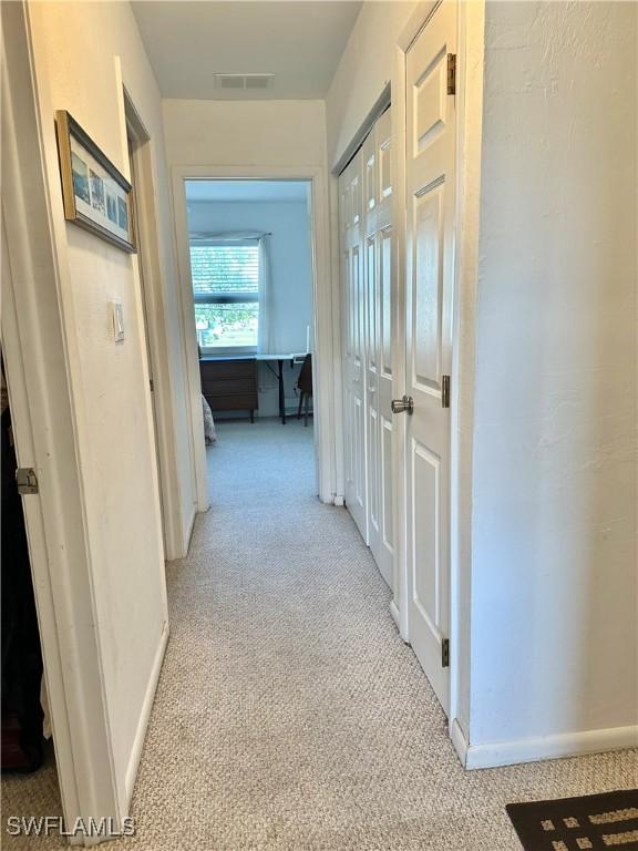 hallway featuring baseboards, visible vents, and light colored carpet