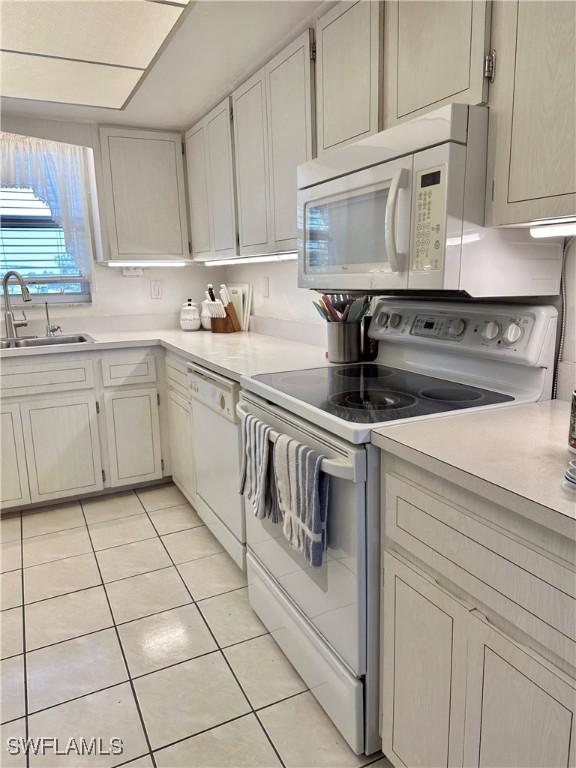 kitchen with light countertops, white appliances, light tile patterned flooring, and a sink